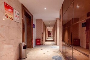 Un corridoio d'hotel con un cestino, una scatola rossa e cartelli indicatori alle pareti.