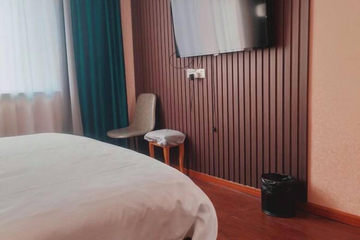 Una camera d'albergo con un letto, una sedia, una TV a parete e un cestino.