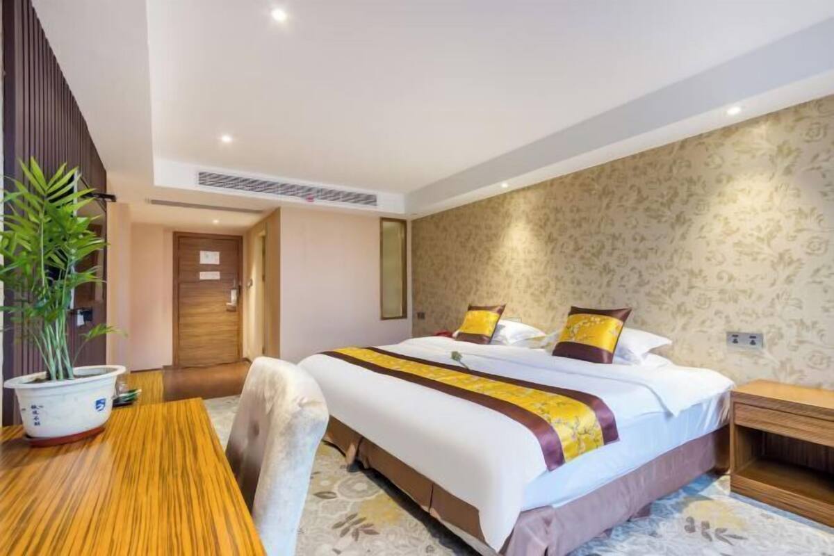 Una camera d'albergo con un letto, un tavolo in legno, una pianta in vaso e un comodino.