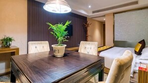 A hotel room with a wooden dining table, four chairs, a potted plant, a bed with a white headboard, and a large window. - Geyue Zhenpin Hotel (Hangzhou)