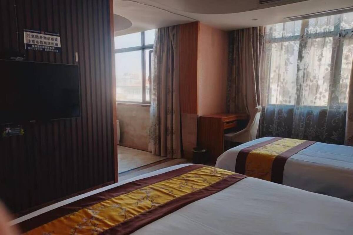 Una camera d'albergo con due letti, una scrivania e un'ampia finestra con tende.