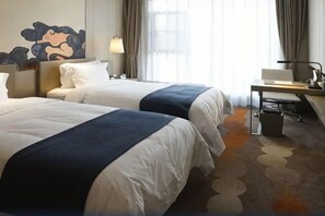 Une chambre d’hôtel avec deux lits, un bureau, une chaise, une lampe et une grande fenêtre avec des rideaux.