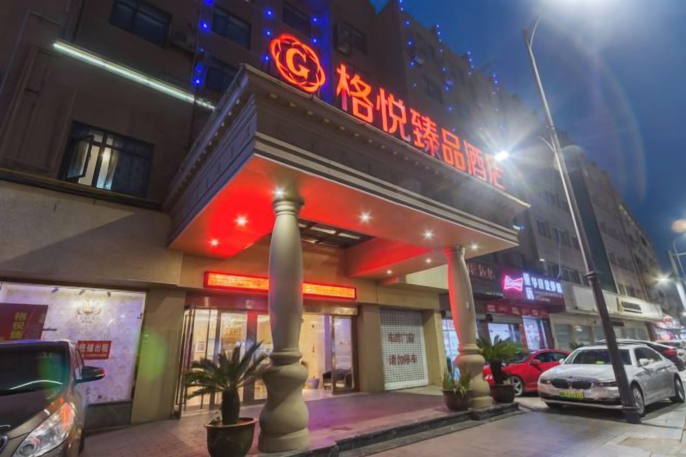 A hotel with a prominent red sign, a covered entrance, and a street view with parked cars.
