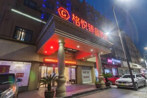 Een hotel met een opvallend rood bord, een overdekte ingang en een straatbeeld met geparkeerde auto's.
