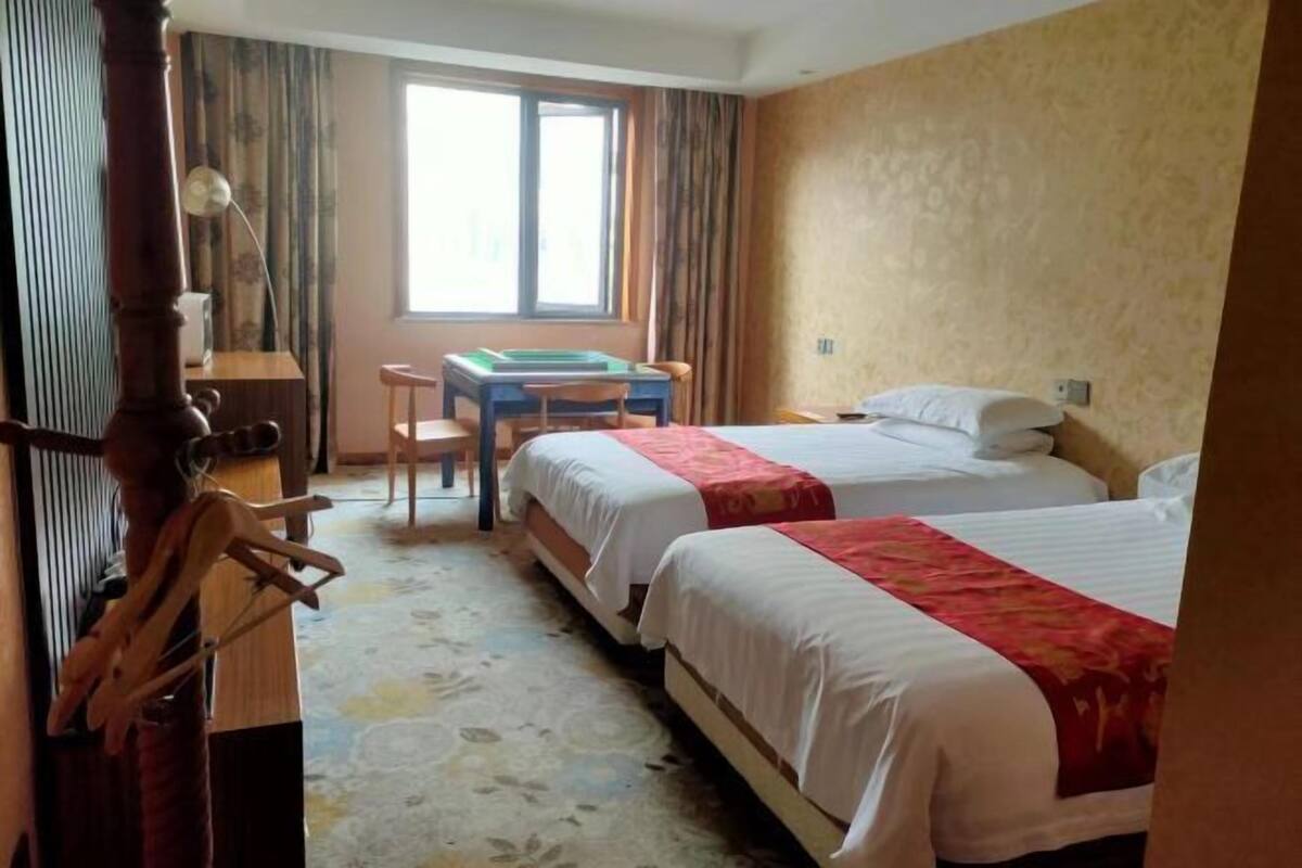 Una camera d'albergo con due letti, una scrivania, una sedia e una finestra.