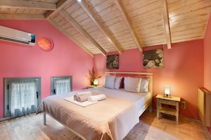 Un dormitorio con techo de madera, cama con almohadas y manta, mesita de noche con lámpara y aire acondicionado de pared.