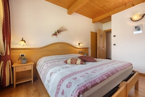 A bedroom with a wooden headboard, a bedside table with a lamp, a bed with patterned bedding, and a wall-mounted light fixture.