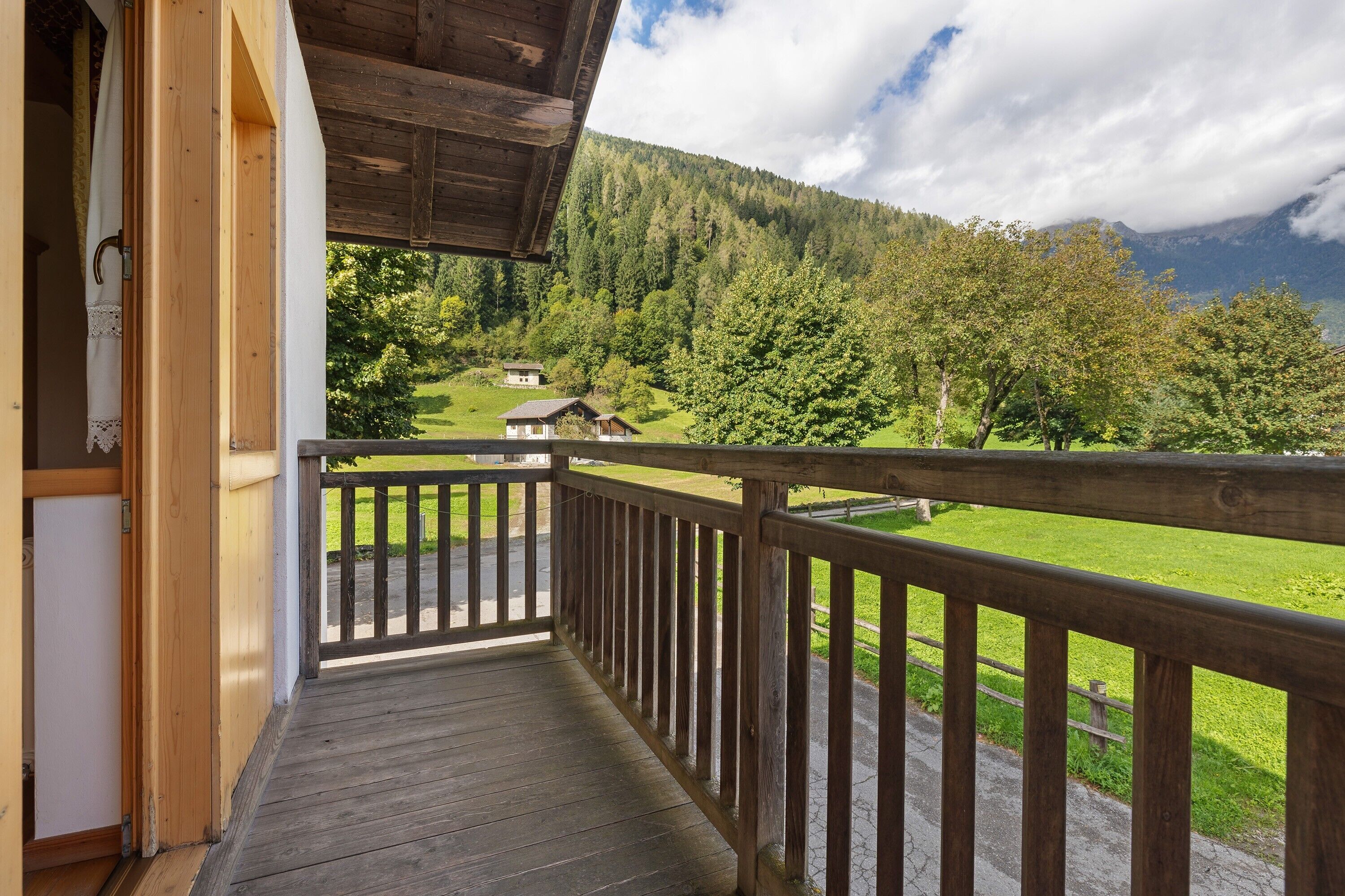 Un balcon en bois offrant une vue sur un paysage montagneux et une petite maison.
