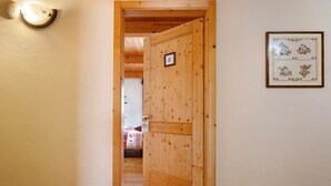 Una puerta de madera que da a una habitación con una cama y una lámpara fijada a la pared.