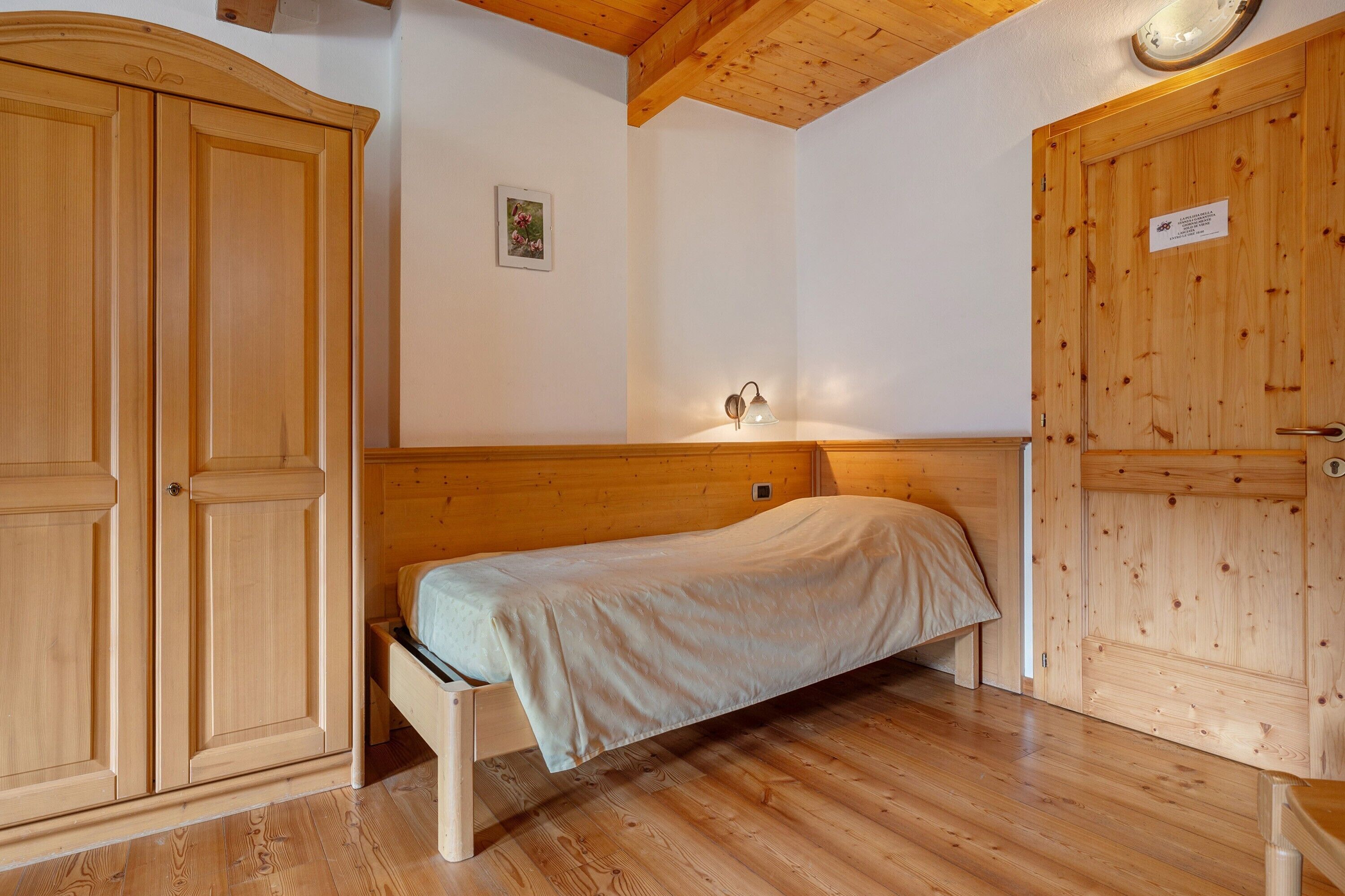 Una habitación de madera con una cama, un armario y una lámpara fijada a la pared.