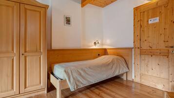 Una habitación de madera con una cama, un armario y una lámpara fijada a la pared.