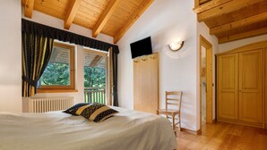 Un dormitorio con cama, una silla, televisión y puertas de madera.
