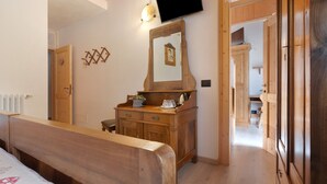 A wooden-framed room with a bed, a dresser, a television mounted above a mirror, and a hallway leading to another room. - Room 'Camera Doppia Comunicante Nonni' with Mountain View, Shared Garden and Wi-Fi (Caderzone Terme)