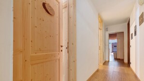 A wooden door, a hallway with a wooden floor, and a white wall with a door at the end.