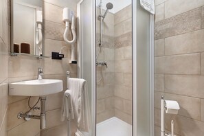 A bathroom with a sink, mirror, towel rack, shower, and toilet paper holder.