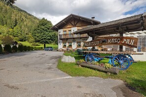 A rustic mountain lodge with a sign reading 'AGRI-TUR MASO PAN,' featuring a wooden exterior, a balcony, and a traditional wooden cart.