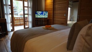 Een hotelkamer met een groot bed, een televisie op een houten standaard en uitzicht op het omliggende landschap door een schuifdeur.