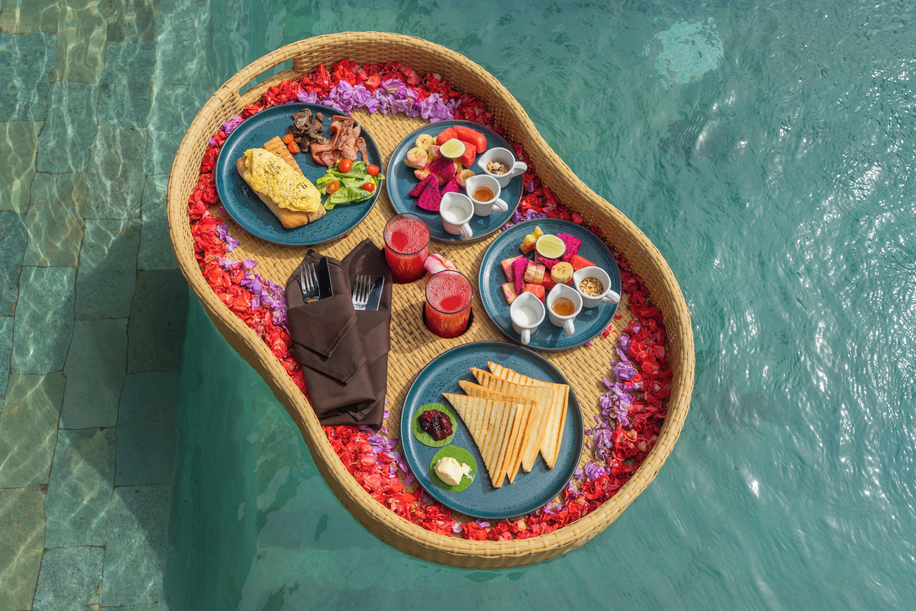 A floating dining setup with plates of food, drinks, and a napkin on a water surface.