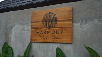 Un letrero de madera con la palabra 'HARMONY' y 'Wooden Villas' sobre una pared gris.