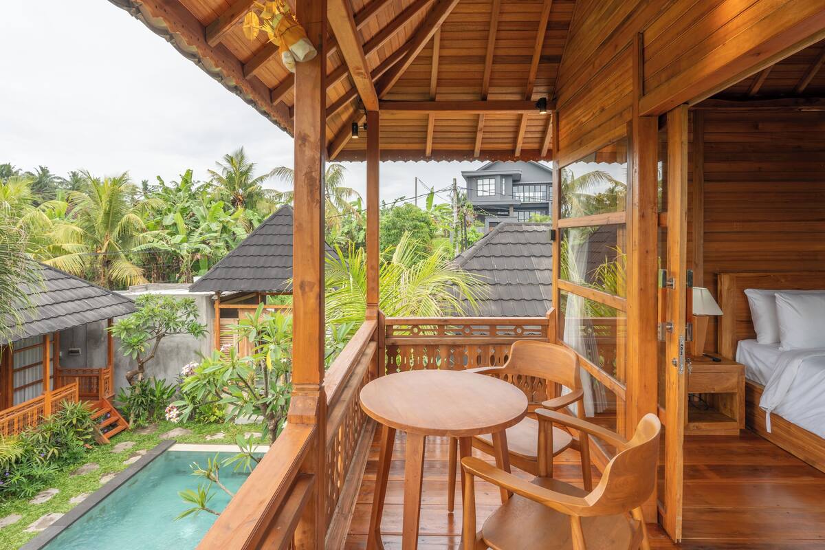 Un balcon en bois avec une piscine, du mobilier en bois et une vue sur le paysage tropical environnant.