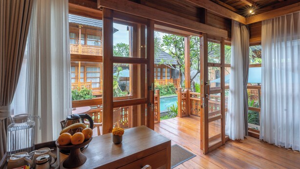 Een houten interieur met een houten tafel, een schaal fruit en een uitzicht op een zwembad en groen buiten.