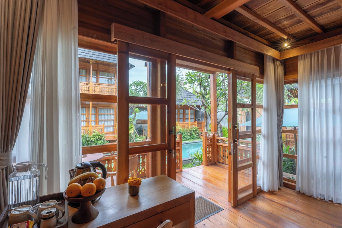 Un intérieur en bois avec une table en bois, un saladier rempli de fruits et une vue sur une piscine et la verdure environnante.