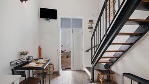 Un escalier avec une rampe en bois et des balustrades en métal noir, un coin repas avec une table et des chaises, et un téléviseur à écran plat fixé au mur.