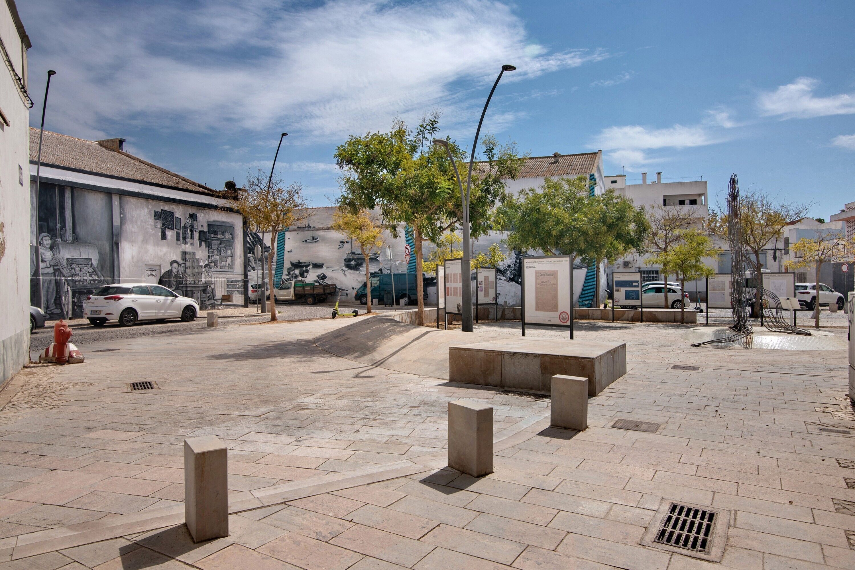 An outdoor urban area with a paved walkway, bollards, and a mural on a building.