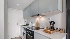 Une cuisine compacte équipée d’un lave-linge, d’une cuisinière, d’un évier et d’un plan de travail sur lequel se trouvent une machine à café et des ustensiles.