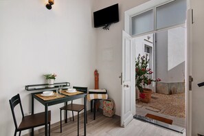 A dining area with a table, chairs, a TV mounted on the wall, and a door leading to an outdoor area with a potted plant.