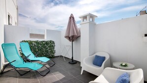 Une terrasse avec deux fauteuils de jardin, une petite table ornée d’une fleur et un parasol.