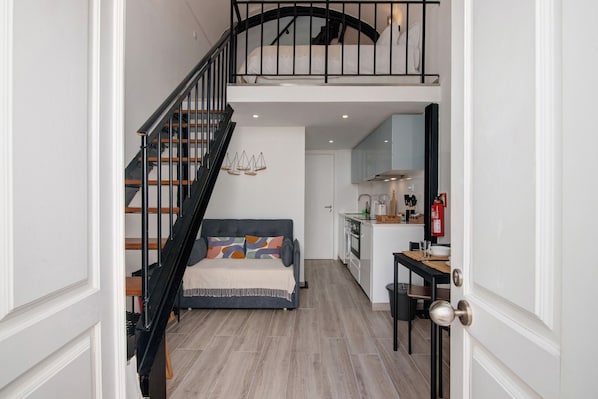 A staircase leading to a loft bedroom with a bed, a dining area with a table and chairs, and a kitchen with cabinets and appliances.