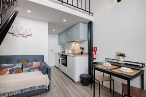 A compact living space with a sofa, kitchenette, dining area, and a staircase.