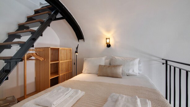 Une chambre à coucher comprenant un lit, une armoire en bois, un portant à vêtements, un escalier et un luminaire fixé au mur.