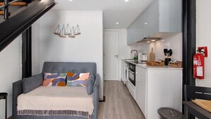 Un espace de vie compact comprenant un lit, une kitchenette et un escalier.