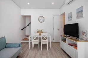 A modern living room with a sofa, dining table, chairs, a TV, and artwork on the walls.