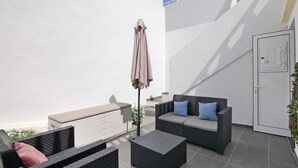 Een moderne zithoek buiten met een bank, twee stoelen, een bijzettafeltje en een parasol.