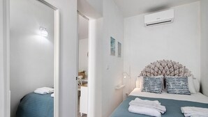 Een slaapkamer met een bed, een nachtkastje, een wandairconditioner en een deur naar een andere kamer.