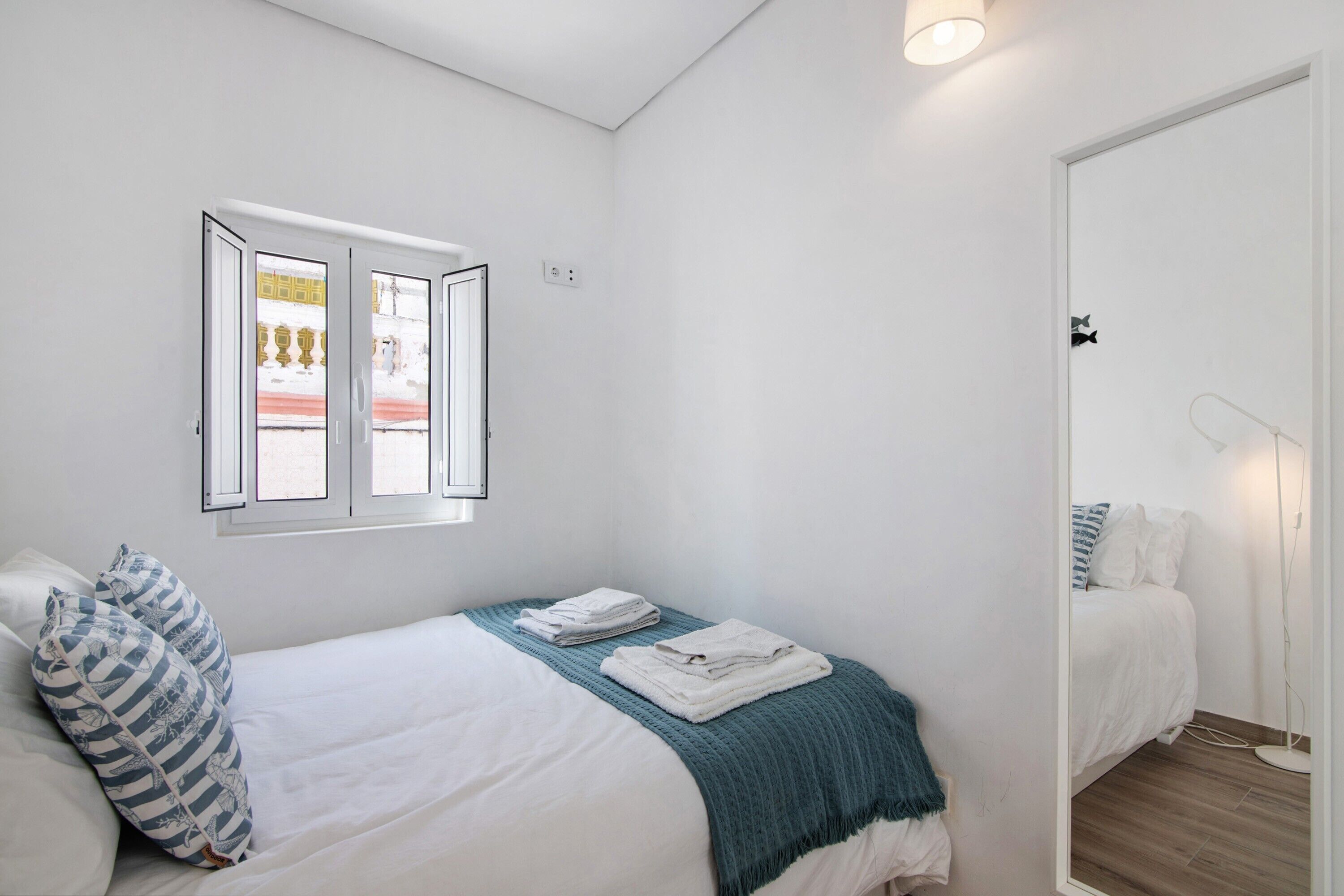 A bedroom with a bed, a window with curtains, a bedside table, and a mirror.