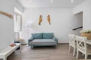 A modern living room with a sofa, a dining table with chairs, a floor lamp, and wall-mounted decor.