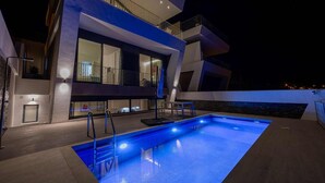 A modern two-story building with a swimming pool, outdoor lighting, and a balcony.