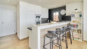 A modern kitchen with white cabinetry, a central island with bar stools, a microwave, and a clock on the wall.