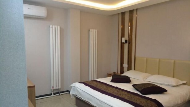 A hotel room with a large bed, two bedside tables, a wooden nightstand, and a wall-mounted air conditioner. - Wanglong Leisure Hotel (Songbei Harbin University of Commerce, Ice & Snow World) (Harbin)