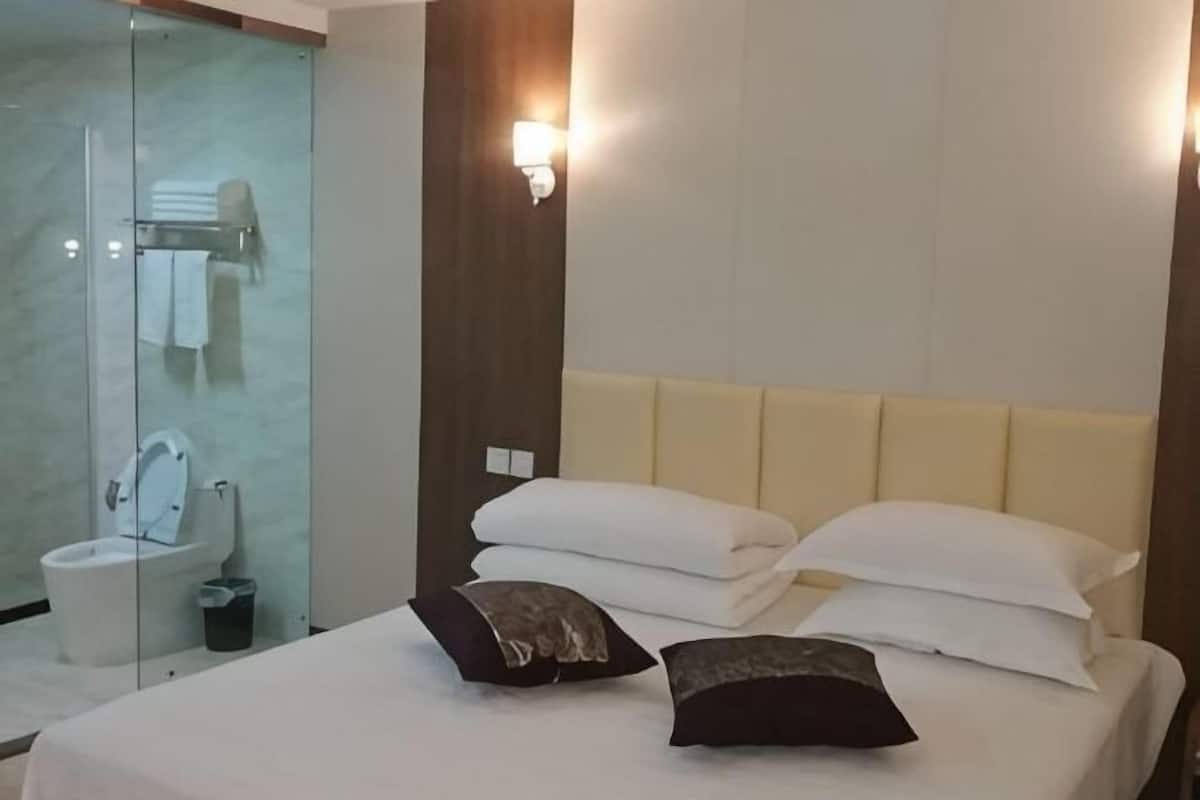 Ein Hotelzimmer mit einem Bett, zwei Kissen, einem Nachttisch, einer Wandleuchte und einer Duschkabine aus Glas.