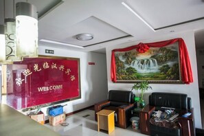 A reception area with a red welcome sign, a painting of a waterfall, and a reception desk. - Gangyue Hotel (Shaoxing)
