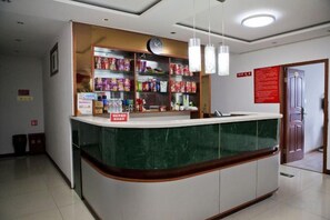Un mostrador de recepción con encimera de mármol verde, un reloj encima y estantes con diversos objetos.