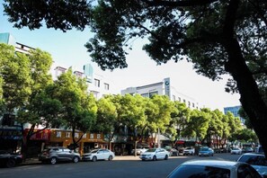 A street lined with parked cars and trees, with buildings in the background. - Gangyue Hotel (Shaoxing)