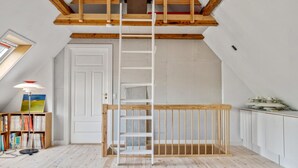 Un dormitorio tipo loft con una escalera de madera, un tapete rojo y naranja, y una estantería llena de libros.