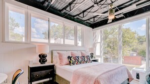 Un dormitorio con una cama grande, una mesita de noche, una silla y una ventana con vistas a árboles.