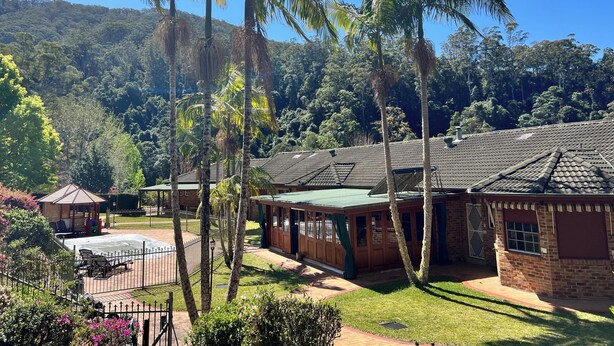 Un resort con varias construcciones, palmeras y montañas al fondo.